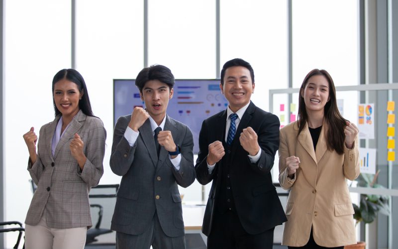Asian business team celebrate corporate victory together in office, laughing and rejoicing, smiling excited employees colleagues screaming with joy in office.